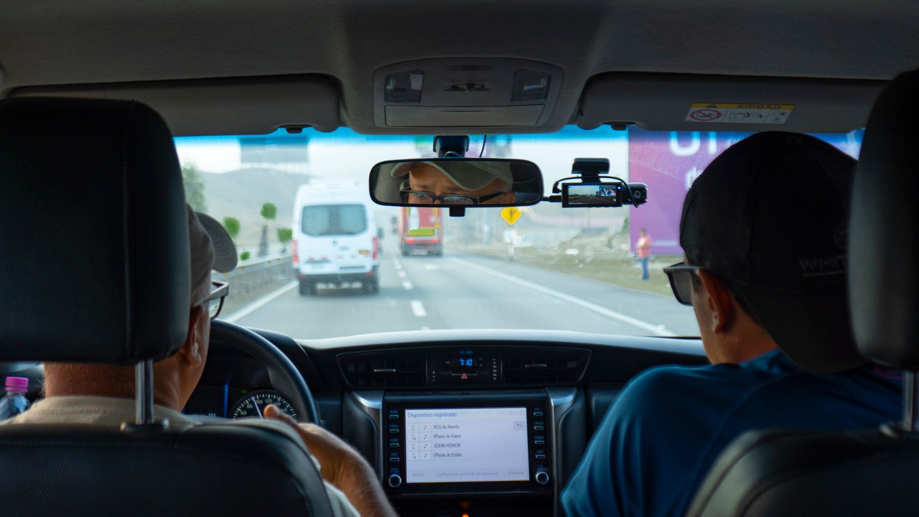 Widok z wnętrza samochodu na autostradę z innymi pojazdami, z kamerą pokładową widoczną na lusterku wstecznym