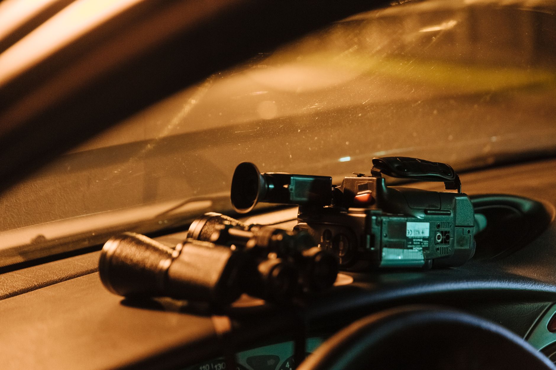Dashcam z zielonym modułem elektronicznym i przewodami leżące na brązowym kokpicie samochodu w oświetleniu słonecznym