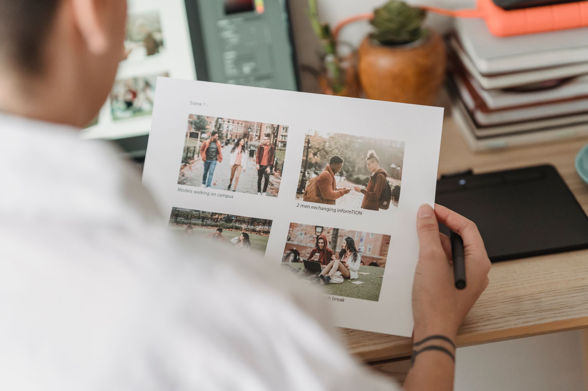 Osoba przeglądająca wydrukowany dokument ze Scene 1 zawierający cztery fotografie pokazujące studentów na kampusie i wymianę informacji.