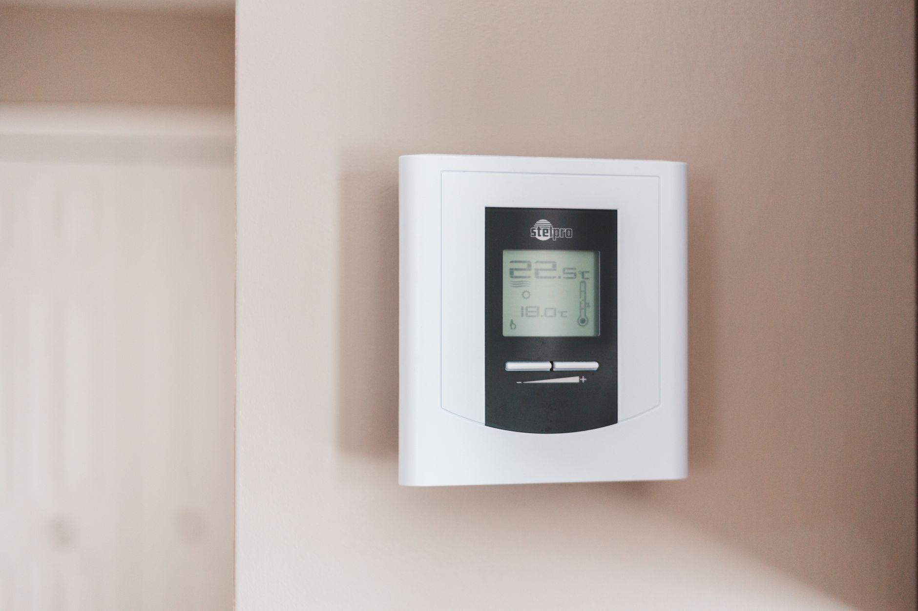 Biały inteligentny termostat ścienny z wyświetlaczem pokazującym 22.5°C i 18.0°C