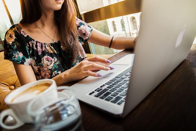 Kobieta w kolorowej bluzce pracująca na laptopie przy filiżance kawy