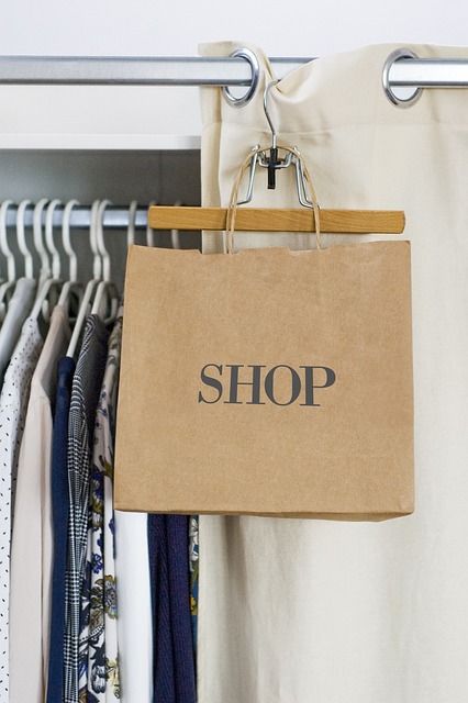 Papierowa torba z napisem SHOP zawieszona na wieszaku do ubrań obok odzieży na stanowisku handlowym