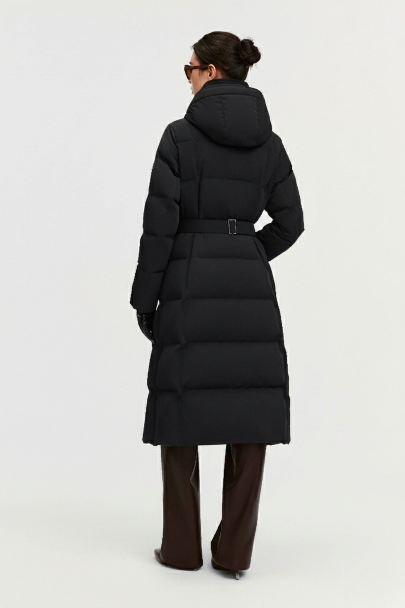 Back view of woman in black puffer coat with hood and waist belt over brown pants