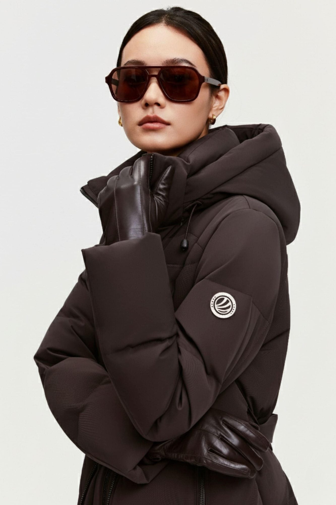 Woman wearing brown puffer jacket with hood and oversized fit, styled with sunglasses and leather accents