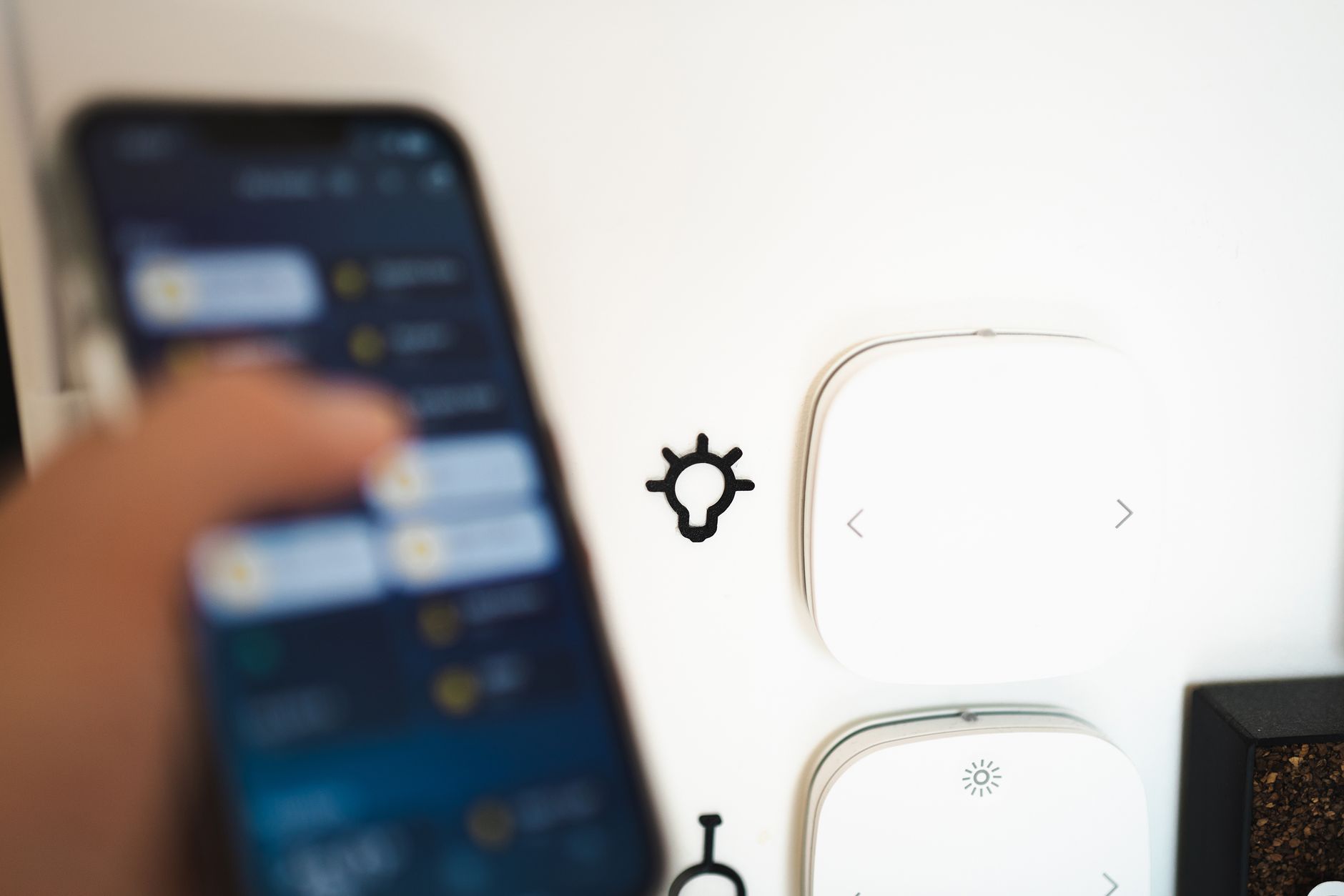 Osoba trzymająca smartphone z aplikacją oświetleniową, w tle widoczne białe urządzenia sterujące