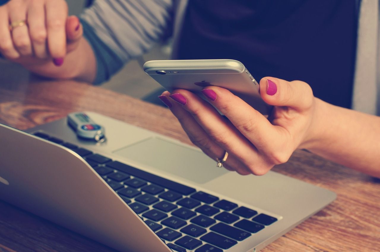 Kobieta z różowymi paznokciami trzymająca smartfon obok laptopa